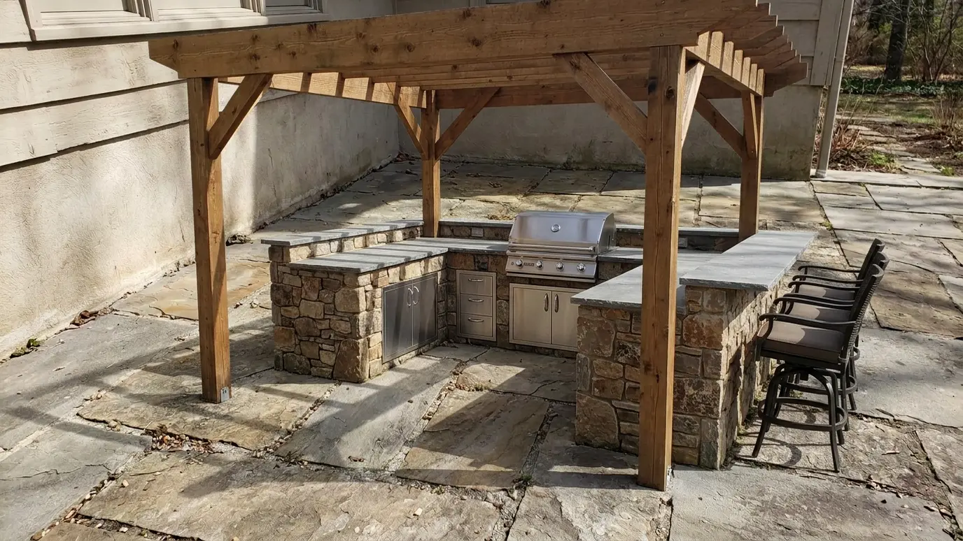 After: a stone patio with a stone grill island with bar seating under a timber pergola